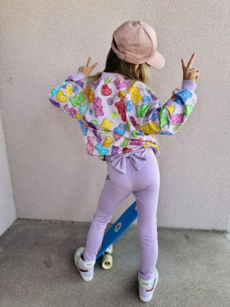 Dziewczynka w bluzie w kolorowe, żelkowe misie i w fioletowych legginsach z kokardą z tyłu